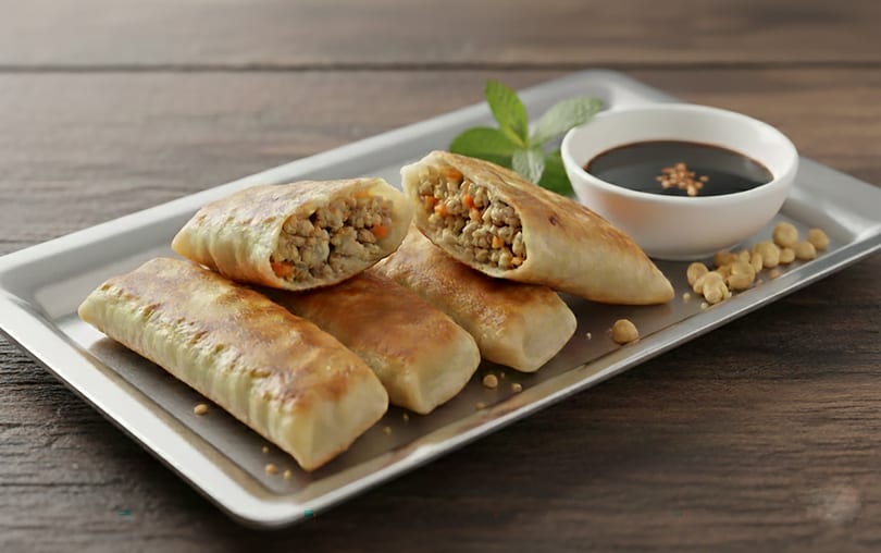 Crispy spring rolls, one cut open to show a savory filling, served with soy sauce.